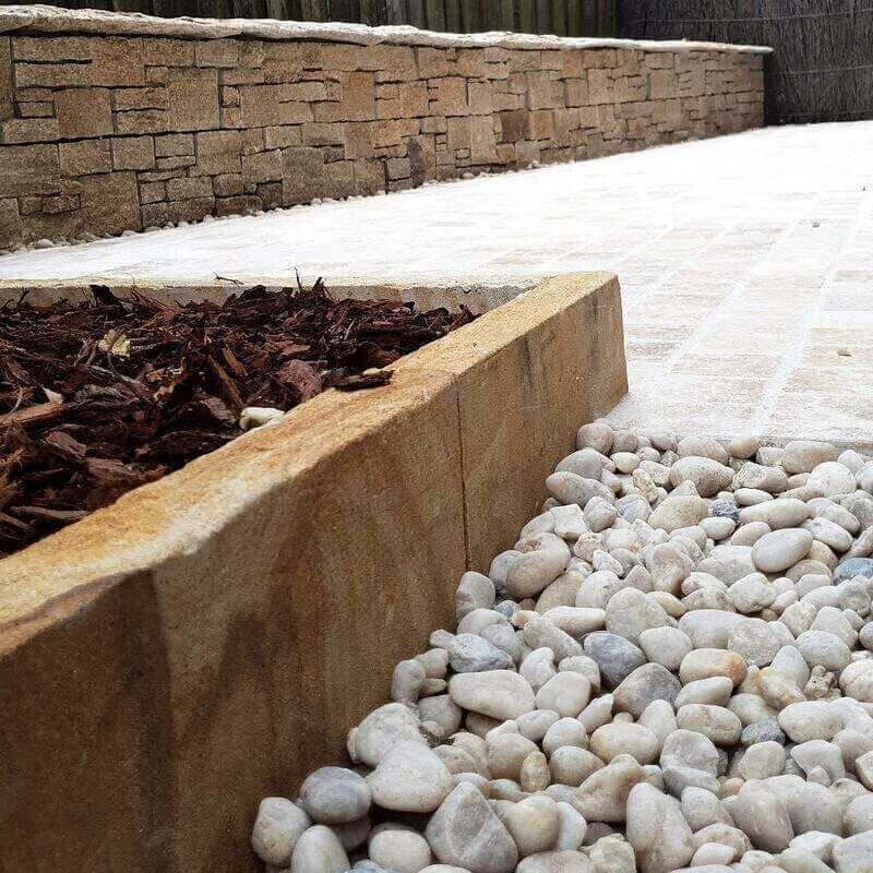 Timber retaining wall beside paving and river pebbles